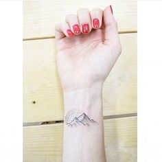 a woman's arm with a mountain tattoo on her left wrist and red nails