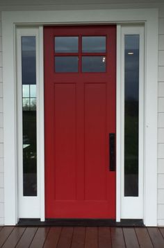 a red front door on a white house with wood flooring and sidelights in the evening