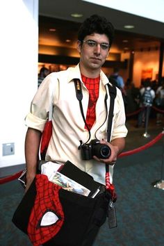 a man dressed as spider - man holding a camera in his right hand and wearing a red tie