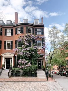 a tall brick building with purple flowers on it's front and stairs leading up to the entrance