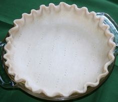 an uncooked pie crust sits in a glass dish on a green cloth covered tablecloth