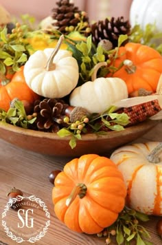 a wooden bowl filled with pumpkins and greenery on top of a wood table