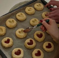 someone is making heart shaped cookies on a baking sheet