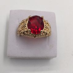 a gold ring with a red stone in the center on a white display stand,