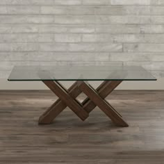 a glass table with wooden legs in front of a brick wall and wood flooring