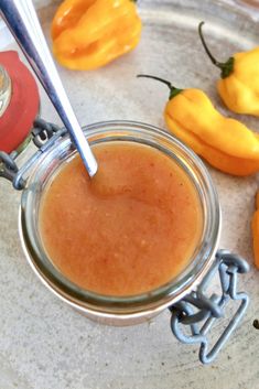 a glass jar filled with orange sauce next to some yellow peppers on a counter top