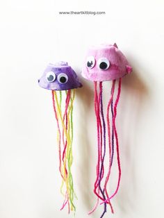 two jelly fish made out of yarn with googly eyes hanging from the side on a white wall