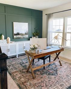 a living room with a large rug and table in front of two windows on either side of the couch