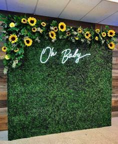 a green wall with sunflowers and greenery in the shape of a baby's name