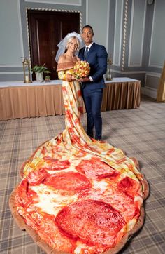 a bride and groom posing in front of a giant pizza