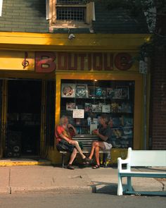 two people sitting on a bench in front of a book store with yellow awnings