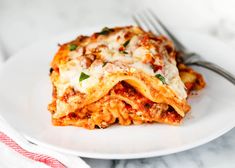 a white plate topped with lasagna covered in sauce and cheese next to a fork