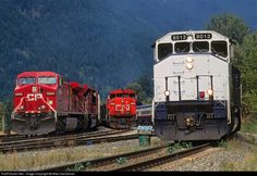 two red and white trains passing each other on train tracks in front of some mountains