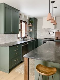 a large kitchen with green cabinets and marble counter tops, along with an island in the middle