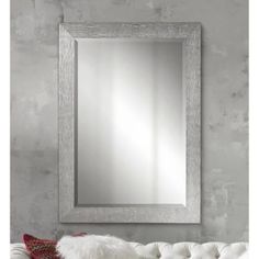 a large mirror hanging on the wall above a white couch in front of a gray wall