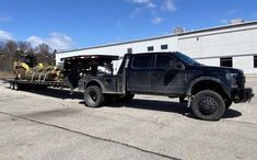 a large black truck is parked in front of a building with a load on it's flatbed