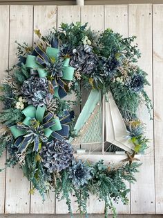 a wreath with blue and green flowers on top of a wooden wall next to a sailboat