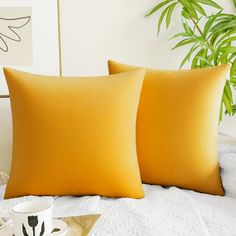 two yellow pillows sitting on top of a bed next to a cup and saucer