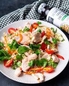 a white plate topped with chicken and veggies next to a bottle of dressing