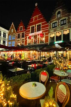 an outdoor dining area with tables and chairs lit up at night in front of buildings