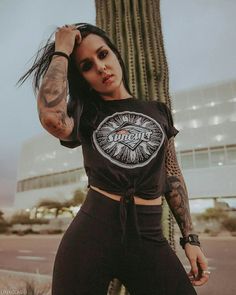 a woman standing in front of a cactus wearing a black shirt and leggings