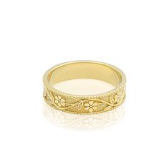 a yellow gold wedding ring with flowers on the side and an engraved design in the middle