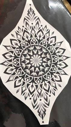 an intricately designed piece of paper sitting on top of a black tablecloth covered in white ink