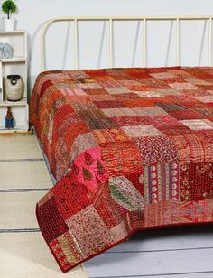 a bed with a red bedspread on top of it next to a white bookcase