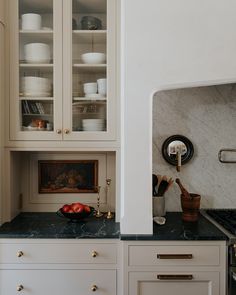 a kitchen with white cabinets and marble counter tops, along with brass pulls on the cabinet doors