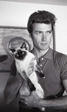 a man holding a siamese cat in his right hand and looking at the camera