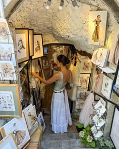 a woman in a white dress is looking at pictures on the wall and holding her arm out