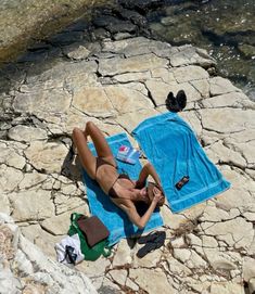 a woman laying on top of a rock next to a body of water with a towel