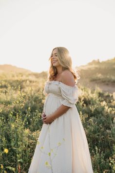 a pregnant woman wearing a white dress standing in a field with wildflowers at sunset