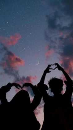 two people making heart shapes with their hands in front of the sky at night time