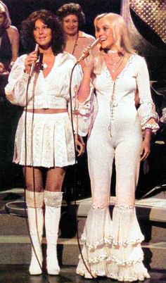 two women in white outfits standing next to each other with microphones on their shoulders