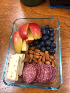 a glass container filled with fruit, nuts and meats on top of a wooden table