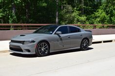 a gray dodge charger parked on the side of a road next to a bridge