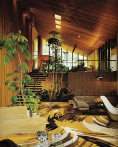 a living room filled with lots of furniture and plants on top of carpeted flooring