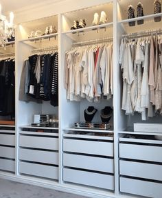 an organized closet with white drawers and hanging clothes on the rails, chandeliers and shoes