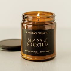 a sea salt and orchid scented candle sits next to a round black lid on a white surface