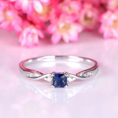 a white gold ring with a blue sapphire and diamonds on the side, surrounded by pink flowers