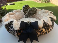 a leopard print dog bed with black bow on the front and side, sitting on top of a white table