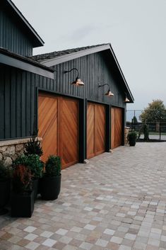 two brown garage doors on the side of a black building next to potted plants