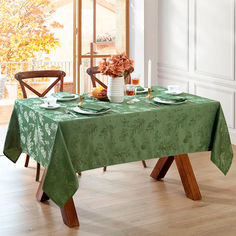 a green table cloth with white flowers and plates on it in front of a window