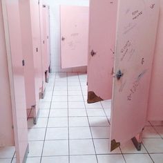 several pink stalls with writing on them are lined up against the wall in a bathroom