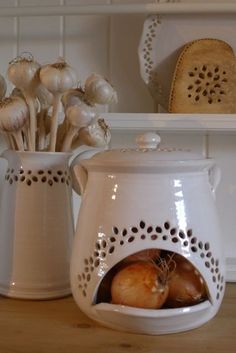 two white vases sitting on top of a wooden table next to garlic and onions