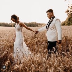 a bride and groom holding hands in a field with tall grass at their wedding day