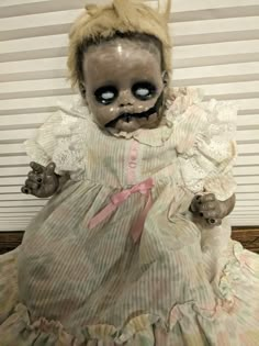 a creepy looking doll with big eyes and long blonde hair wearing a dress that has been made to look like it is sitting on a bed