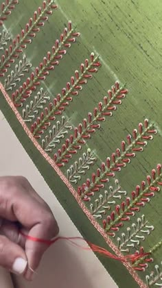 someone is working on an embroidered piece with red thread and green fabric in the background