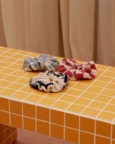 three crocheted hair clips sitting on top of a yellow tiled counter next to a window